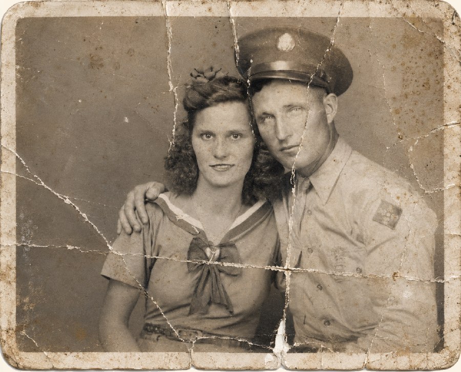 A badly cracked and faded vintage photograph of a couple, damaged by decades of age.