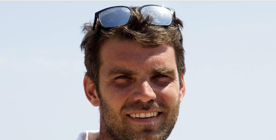 A casual phone snapshot of a man with harsh overhead lighting and an unposed expression.